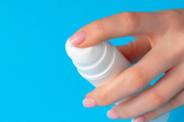 Female hand holding skincare product bottle on blue