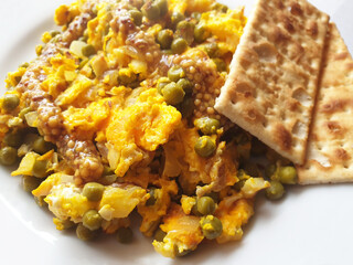 A light breakfast of scrambled eggs and peas drizzled with Dijon mustard. Macro scrambled eggs with cracker.