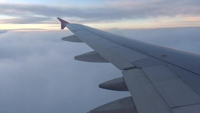 View of a plane wing while flying in the air over the clouds in the early morning