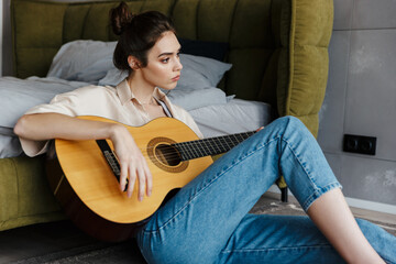 Image of young caucasian brunette woman playing acoustic guitar at home