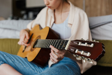 Image of young caucasian woman playing acoustic guitar at home