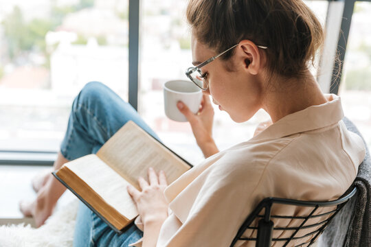 Image of thinking cute woman reading book and drinking coffee