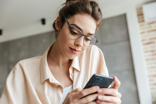 Image of pleased woman using mobile phone while sitting on couch