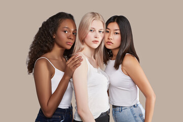 The real beauty exists in every corner of the world and is presented by women of all races. Three beautiful ladies with different skin and hair colour are dressed in jeans and white tank tops.