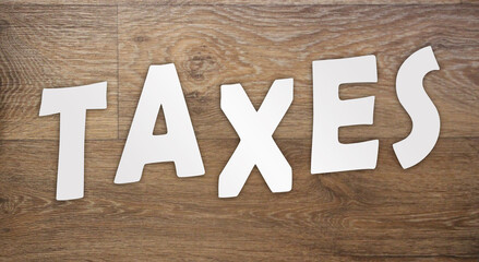Taxes word letters cut from white paper on wooden background. Taxes, fees and penalties business...