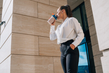 Beautiful woman about to drink coffee from a shaker, walking near office buildings.