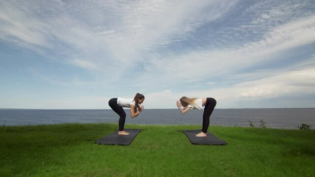 Two young women practicing meditation and yoga in nature at high mountain cliff near the sea.