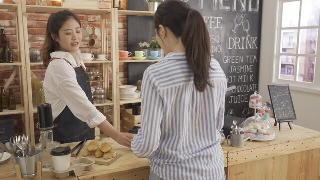 waitress using tablet working in cafe greeting regular customer recommend dessert in counter. asian woman barista serves croissant and coffee to go ordered to client. concept of restaurant business
