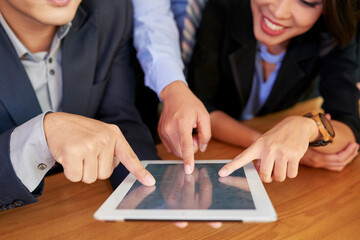 Group of three business people working together using tablet computer, touching screen with their...