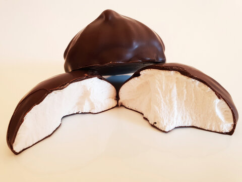 A whole marshmallow and a broken marshmallow on a white surface. Macro.
