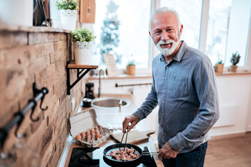 Portrait of a smiling senior man cooking food at home, looking at camera.