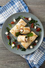 Pancakes with spinach, feta and dried tomatoes. Served on a gray plate. Wooden natural background.