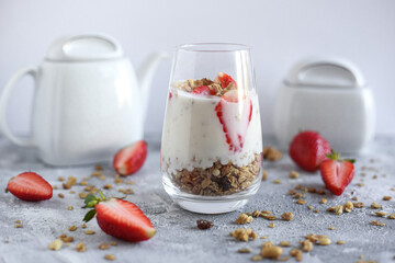 yogurt dessert with oatmeal, walnut and strawberries on light grey table with tea set and half strawberries. Health food. 