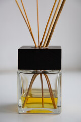 close-up glass diffuser with a black cap, wooden sticks and yellow aromatic oil. white wall in the background. selective focus
