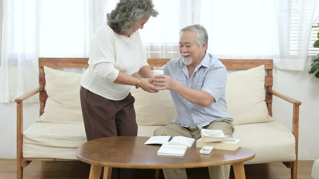 Asian elder wife give a cup of milk to her Asian husband. Elder healthy, Good food good mood, happy retirement concept.