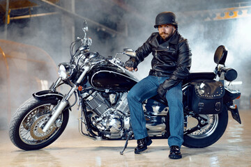 Biker man in leather jacket and helmet sitting on his motorcycle