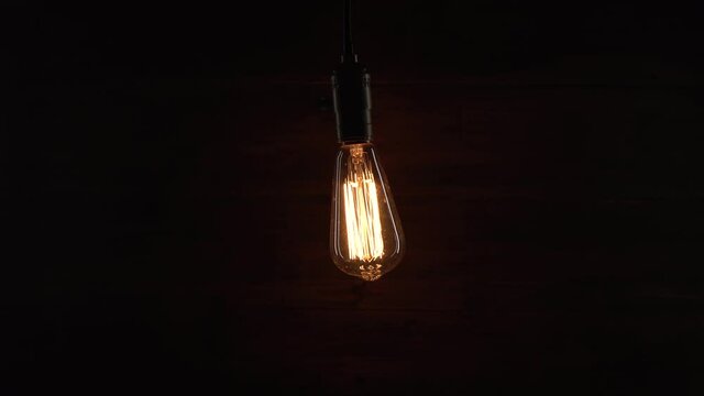 Man turn on and off an old retro lamp with his hand on wooden background. Man enters barn or old mansion and turns on vintage lamp hanging from the ceiling.