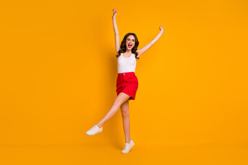 Fototapeta na wymiar Full length photo of funny cheerful lady raise hands one leg weekend sunny weather summer wear casual white tank-top red mini skirt shoes isolated yellow bright color background