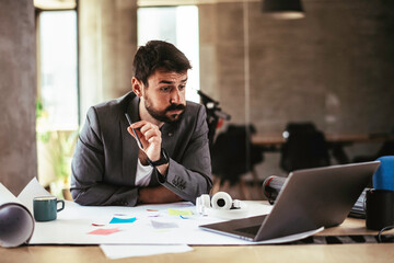 Obraz premium Portrait of handsome businessman in office. Tired businessman working on laptop in office . 