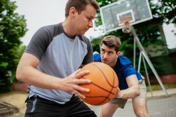 Two young men playing basketball in the park. Friends having a friendly match outdoors