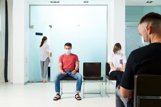 Young people in medical masks, sitting in a queue and waiting for a doctor's appointment in the hospital.