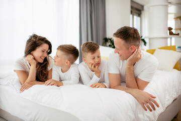 Fototapeta premium Young family enjoying in bed. Happy parents with sons relaxing in bed. 