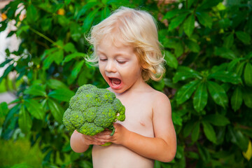 Little blond boy eating broccoli.