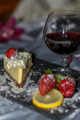 Piece of cake with chocolate and delicate lemon cream and strawberrys. A glass of red wine with strawberries and oranges shared with a loved one