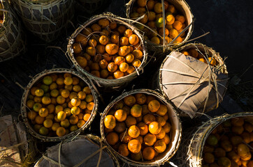 Fresh mandarin oranges fruit or tangerines in wicker bamboo baskets for sell at Zay Cho Market in Mandalay, Contrast photo with dark shade