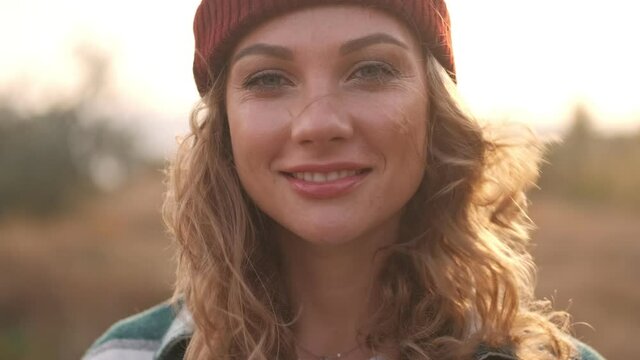 Close up view of smiling blonde woman wearing hat and plaid shirt posing and looking at the camera outdoors