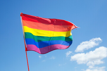 Rainbow Flag at a Gay Pride Parade with a blue sky background.