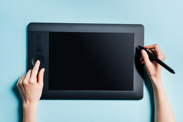 Top view of man holding stylus and using drawing pad on blue surface