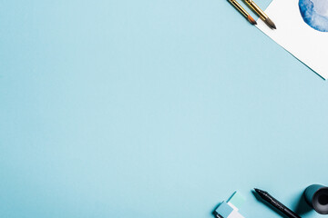Top view of paintbrushes near watercolor drawing and stylus of graphics tablet on blue background