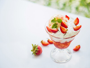 Close up side views a cup of delicious strawberries sundae with mint leaves on a white table next to the glass window through nature background in the afternoon.