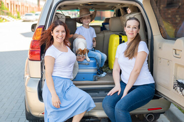 Happy same-sex family going on a car trip around the country. Lesbian couple with son and dog are loading luggage in the trunk and is ready for summer vacation. Independent travel.