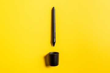 Top view of stylus of graphics tablet and stand on yellow surface