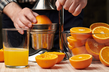 Squeezing an orange with a manual press, close view, making a glass of fresh. Fresh oranges on a...