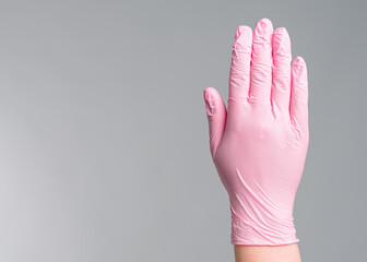 Close-up doctor's hand in pink rubber gloves shows a stop gesture on grey background.