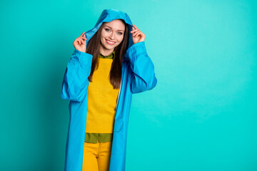Photo of attractive pretty funny lady cheerful mood rainy weather street walk hold hood head toothy smiling wear casual outfit raincoat sweater pants isolated teal color background