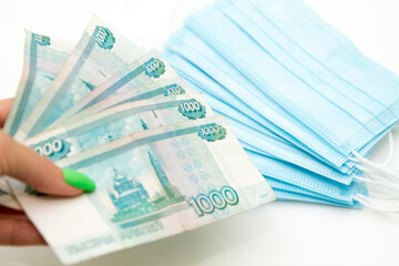 woman's hands holding a hip of russian 1000 rubles banknotes in front of blue medical masks as expenses concept during coronavirus covid19 pandemic