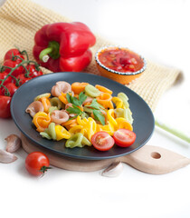Colorful pasta with tomatoes, garlic, parsley, pepper on a black plate. Pasta for child with tomato sauce on a white background
