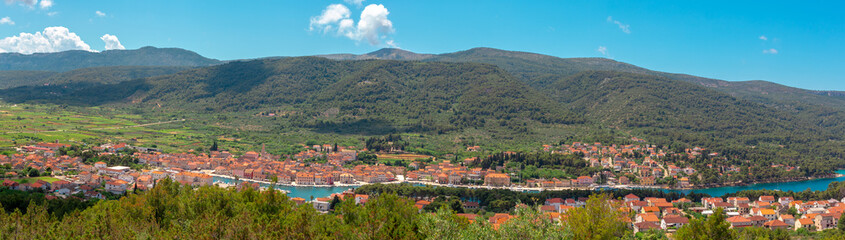 Fototapeta na wymiar Wide picturesque panorama of Starigrad town on the island of Hvar. Seen from a nearby hill. Town buildings seen stretching from the harbour entrance to the city center