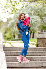 Young smiling woman in denim suit holds baby girl