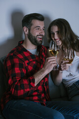 happy young couple laughing while sitting on sofa and holding glasses of white wine