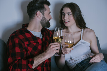 happy young couple sitting on sofa, looking at each other while holding glasses of white wine
