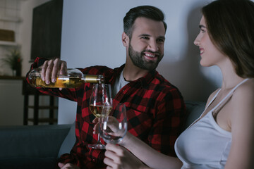 happy girl holding glasses while cheerful man pouring wine