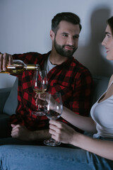 handsome man pouring white wine into glass near happy girlfriend
