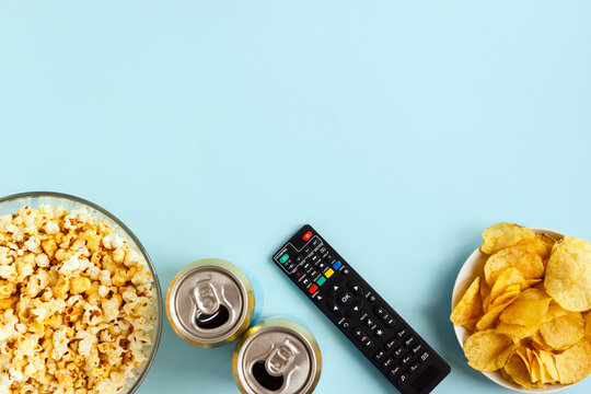 TV remote control, snacks and cans of beer on a blue background. Concept of a family watching a movie and television. Selective focus, layout, top view, place for text.