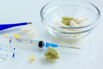 Multicolored pills, tablets against the virus, flu, disease, a thermometer and a syringe on light...