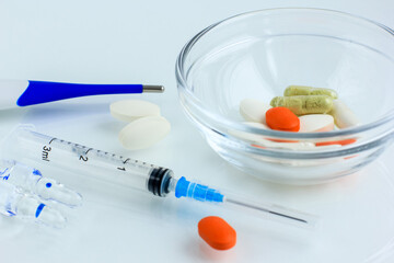 Multicolored pills, tablets against the virus, flu, disease, a thermometer and a syringe on light...